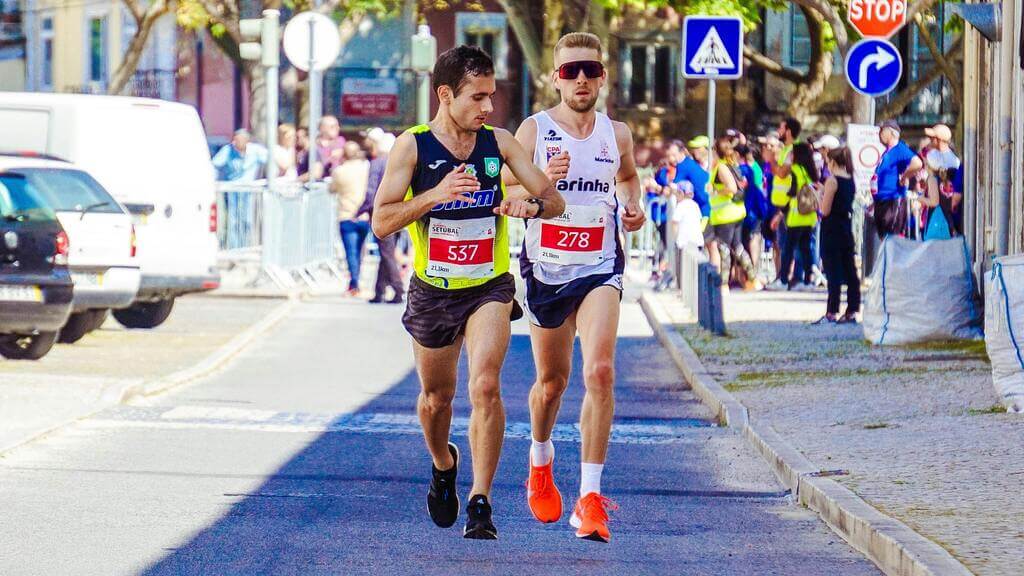 Deux coureurs en plein marathon, l’un vérifiant sa montre connectée pour ajuster son effort, l’autre maintenant son rythme dans un cadre urbain.