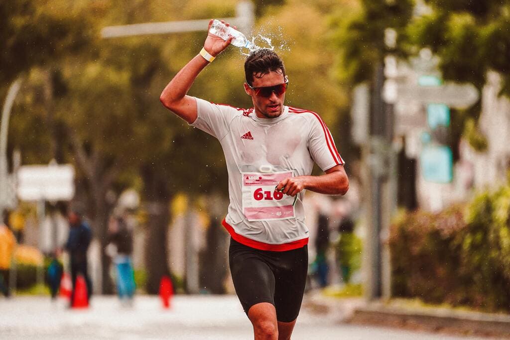 Coureur se rafraîchissant avec de l’eau pendant une course pour lutter contre la chaleur et gérer l’effort.